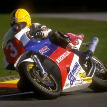 Joey Dunlop pilotando su Honda #3, inclinado en una curva cerrada, con su característico casco amarillo.