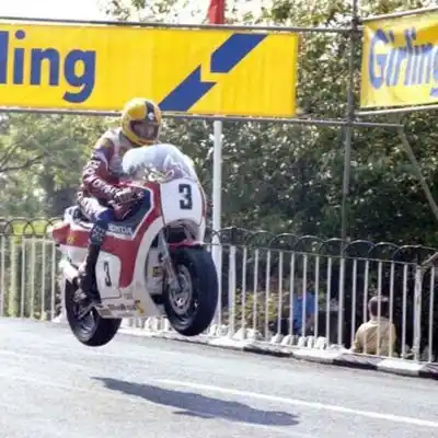 La Época Dorada de Joey Dunlop en el TT Joey Dunlop y su Honda #3 elevándose por un salto en la carretera durante el TT de la Isla de Man, mostrando su dominio.